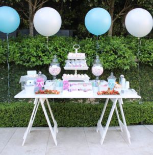 White painted trestle table outside with balloons and cakes on top