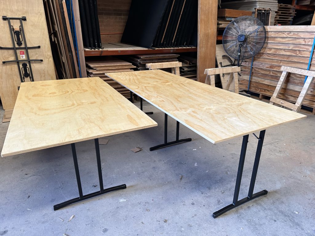 Two folding trestle tables setup side by side with one table having two legs and the other having three legs