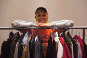 Woman standing behind clothing rack with various shirts hanging