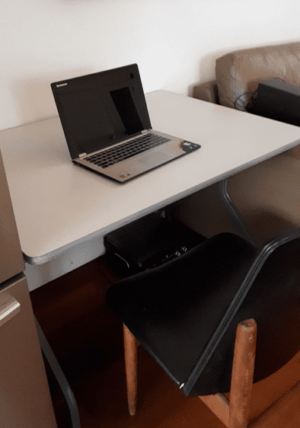 Small grey melamine folding table with a laptop on the surface and a chair in between the legs