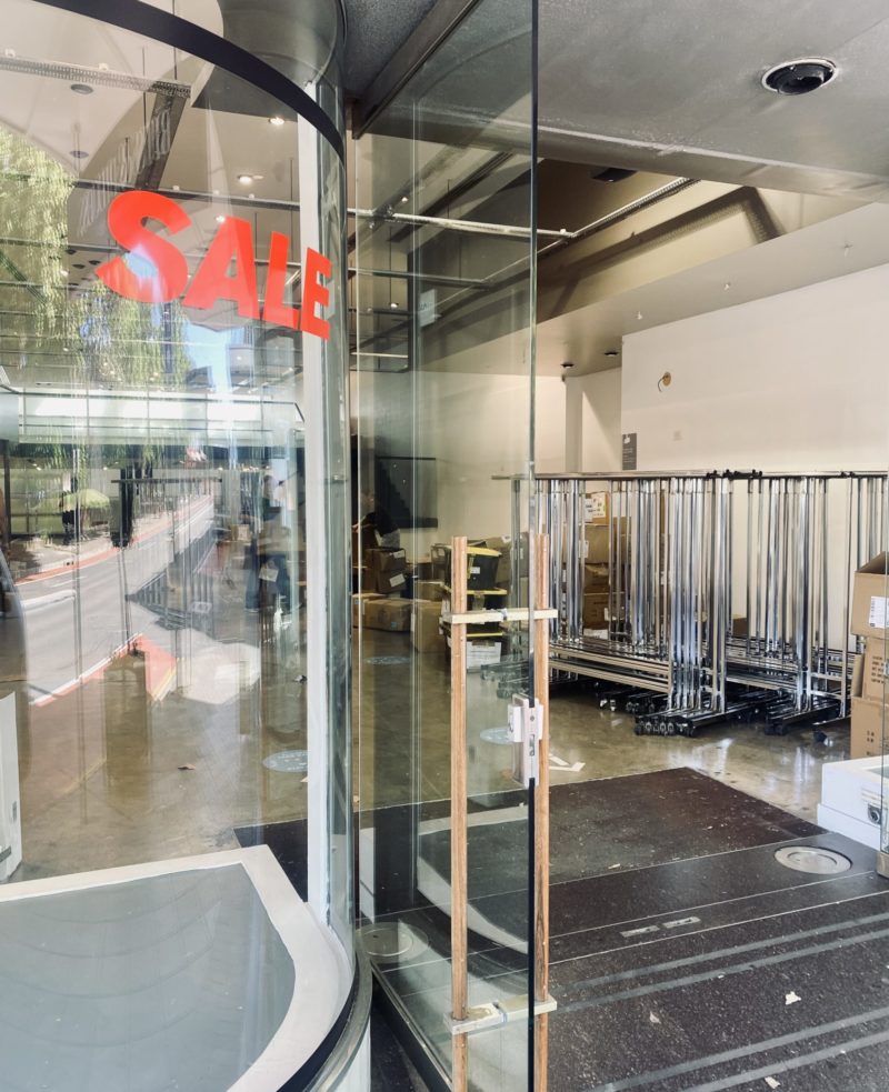 Looking into a pop up store with clothing racks in the background and a SALE sign on the glass window